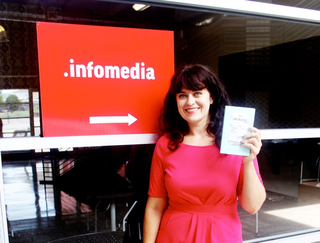 Carrie holding a flyer next to an Infomedia sign