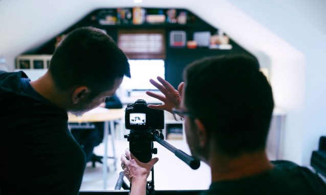two men adjust a video camera in a well lit studio