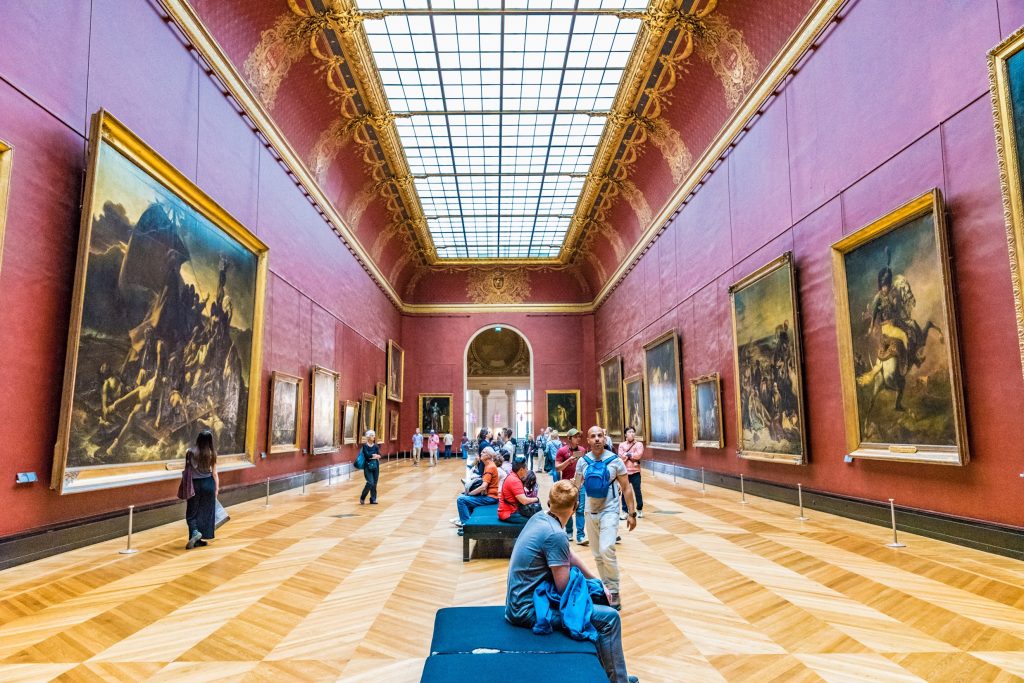 people walking around an art museum with multiple paintings displayed