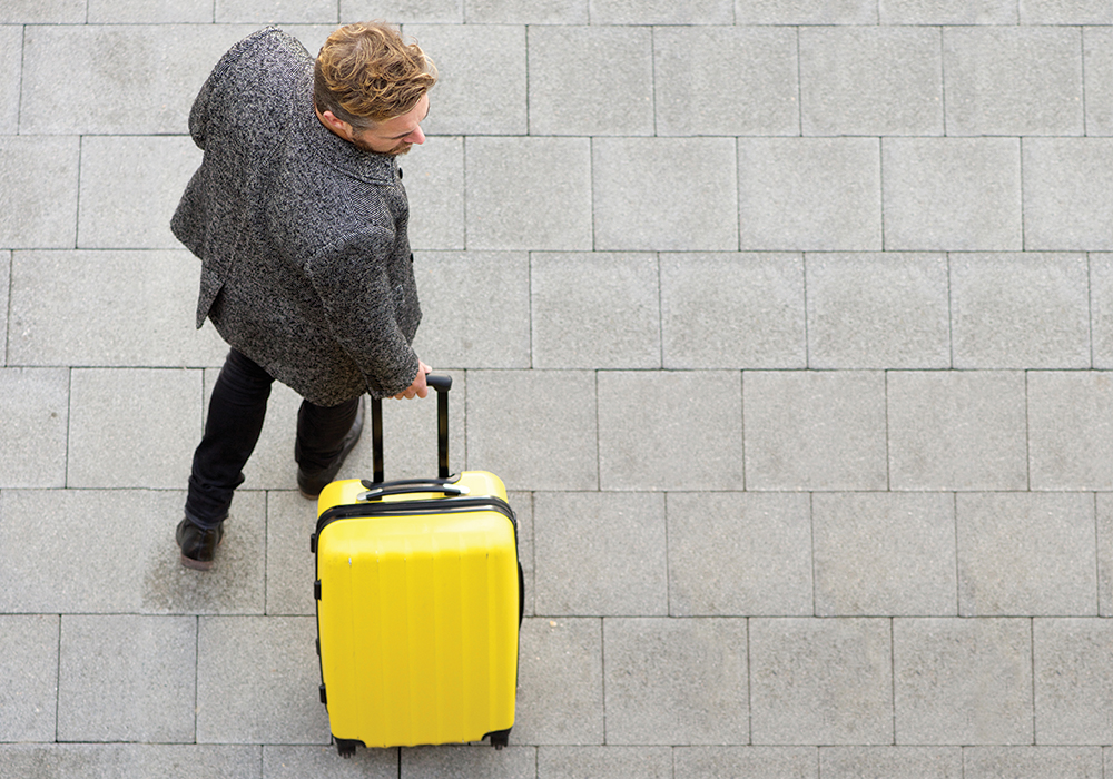 man carries bright yellow suitcase
