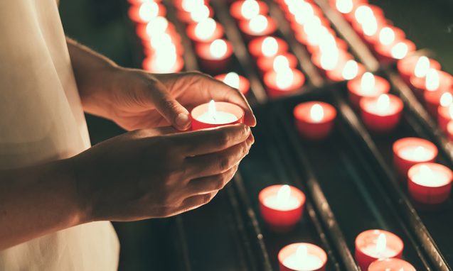 woman holds a lit votive candle in a church
