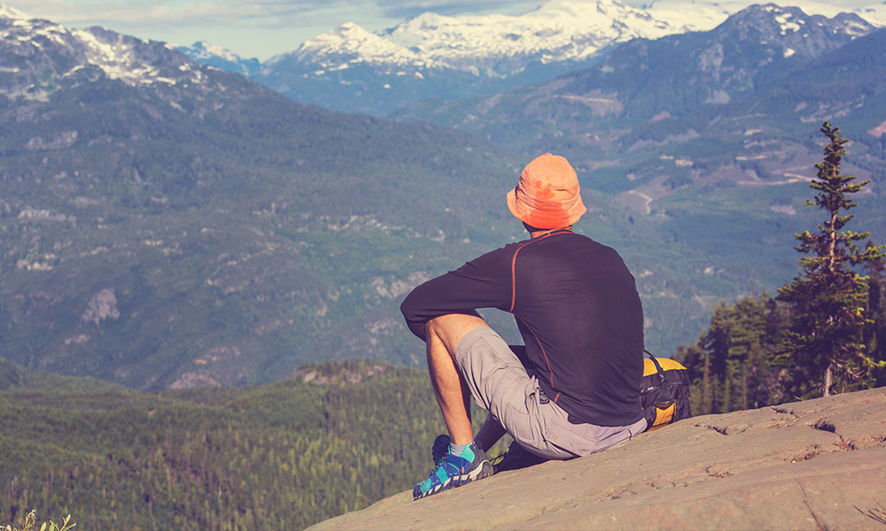 man sits on top of a mountain and looks out on a sunny day