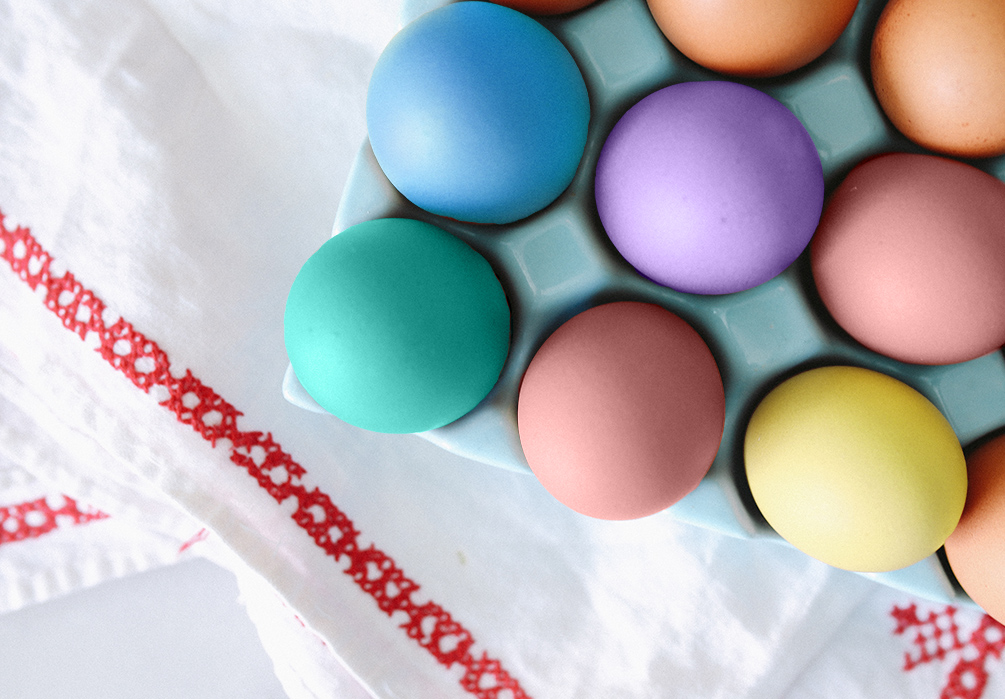 Pastel Easter eggs rest in a carton placed on white dishcloths trimmed in red