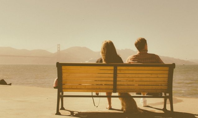 A man and woman sitting on a bench together overlooking the golden gate bridge