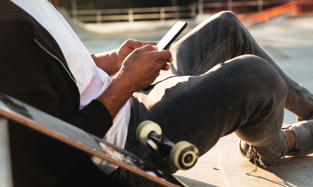 man leaning next to a skateboard and using a cell phone