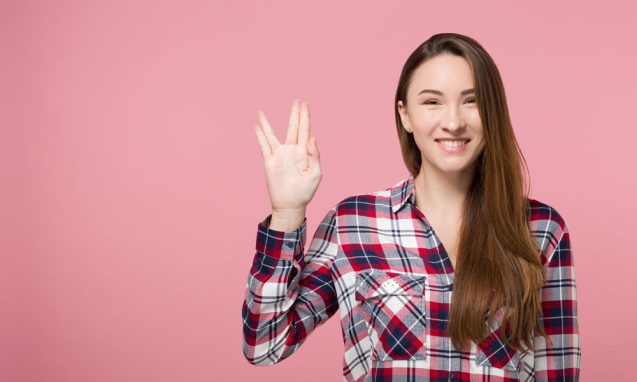 woman makes the Vulcan salute on a pink background