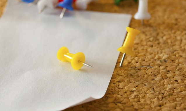 thumbtacks pinning a white piece of paper on a corkboard