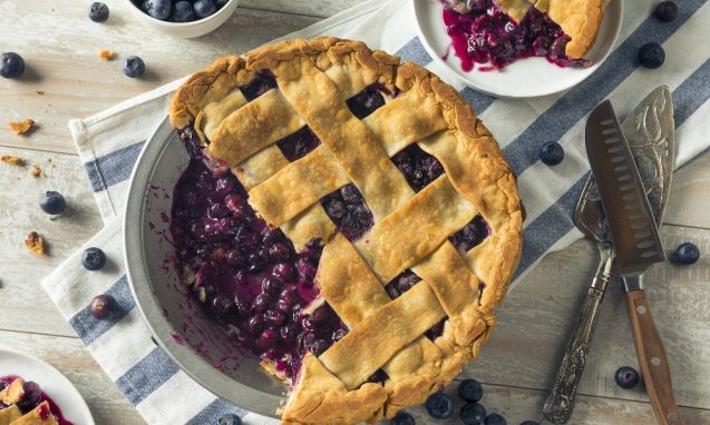 cut blueberry pie with lattice crust on top of a checkered cloth
