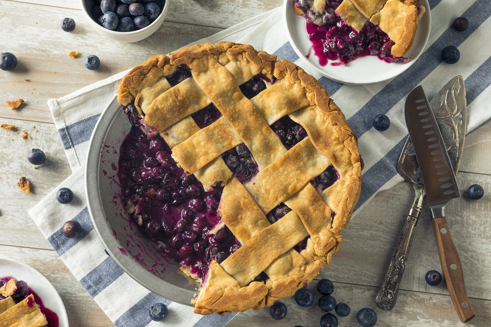 cut blueberry pie with lattice crust on top of a checkered cloth