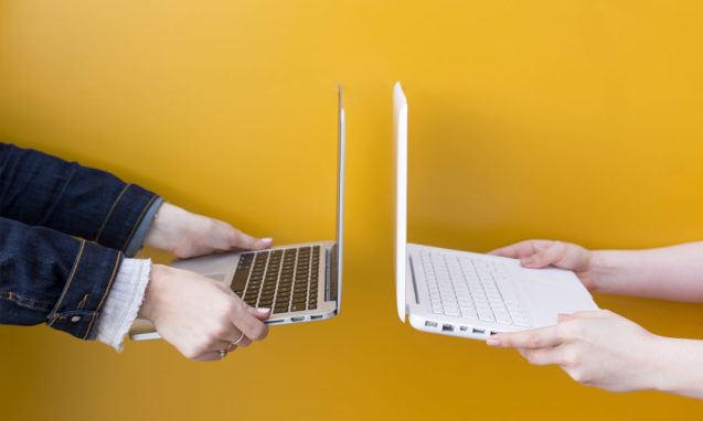 two women hold laptop computers