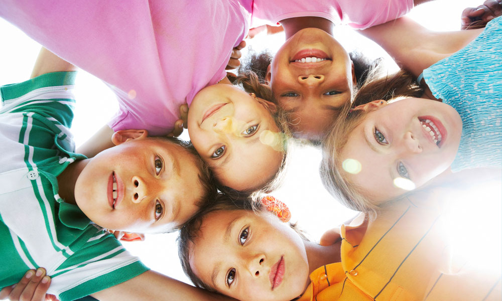 five school-age kids huddle in a circle on a sunny day