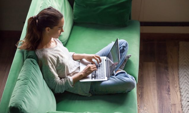 young woman using a laptop sitting on a green sofa