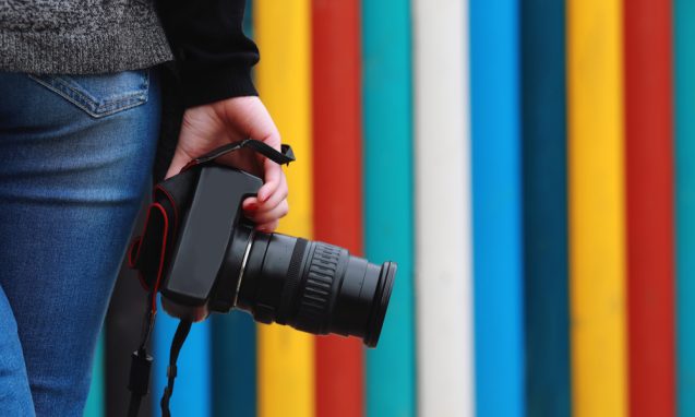woman's hand holding a DSLR camera in front of a colorful striped wall