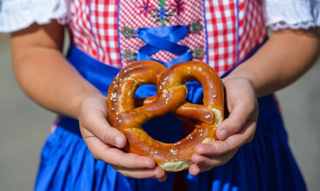 small girl wearing traditional German clothing holding a pretzel