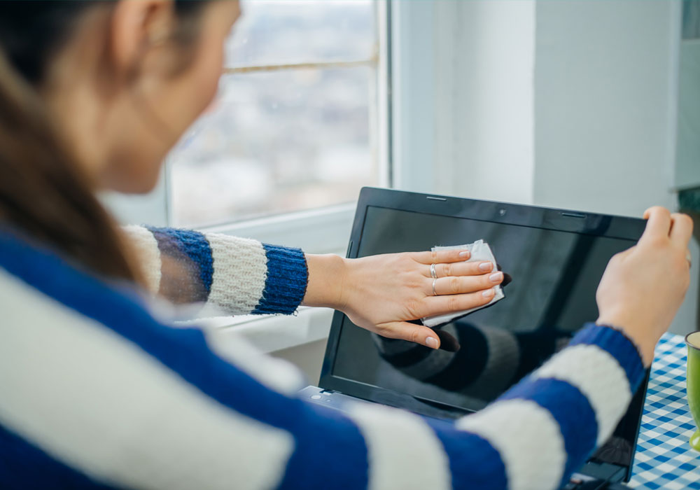 a woman cleaning her monitor screen with a wet wipe in her home office