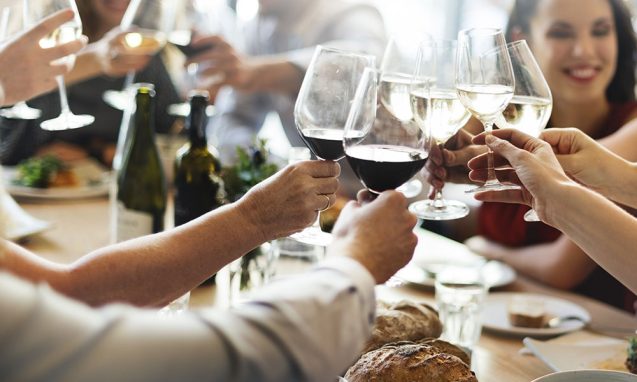 Ten people seated at a table featuring loaves of bread and salads raise wine glasses over their meals