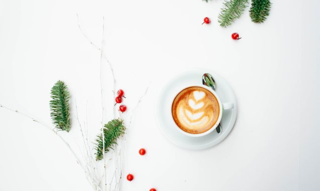overhead view of a cup of coffee and sprigs of fir tree and red berries on a clean white table